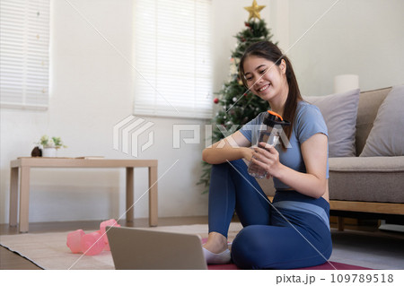 Young Asian woman using laptop and drinking water while doing yoga exercise at home. relax time 109789518