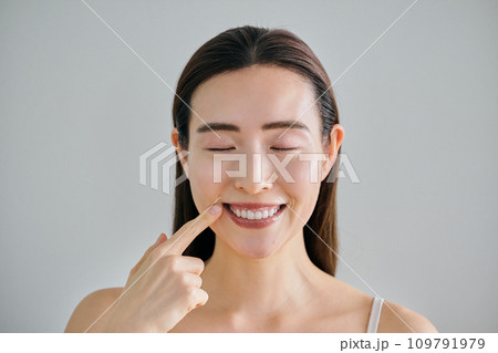 口元を指さす白い歯の30代女性 口元を指さす白い歯の30代女性 109791979