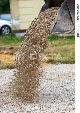 a bulldozer pours macadam from a bucket onto the ground at a construction site - close-up view 109792302