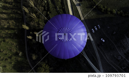 Aerial view of a blue balloon in the sky over the countryside area, France. Shot. Flying above trees, bushes, green fields, and park cars. 109793701