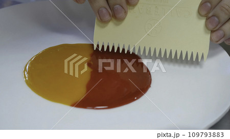 Smearing jam on a plate. Two kinds of jam smeared on the plate with a spatula 109793883