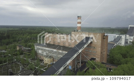 Old red industrial factory building with tall smokestack against grey rainy sky. Aerial view 109794017