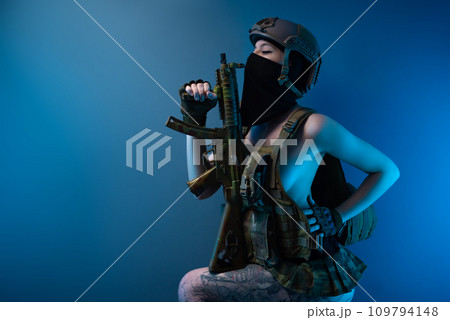 sexy girl soldier in a helmet, armed with an automatic rifle, in military clothes on a blue background sexy girl soldier in a helmet, armed with an automatic rifle, in military clothes on a blue background 109794148
