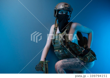 sexy girl soldier in a helmet, armed with an automatic rifle, in military clothes on a blue background 109794151