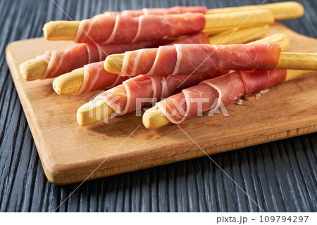 Parma ham prosciutto with Italian grissini breadsticks on a black wooden table . 109794297