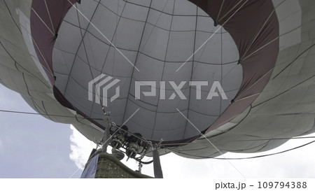 Close up of a hot air balloon flying in the sky. Flying-up balloon with a basket against the blue sky the bottom view Close up of a hot air balloon flying in the sky. Flying-up balloon with a basket against the blue sky the bottom view 109794388