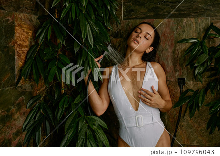 Sensual woman taking invigorating shower surrounded tropical foliage 109796043