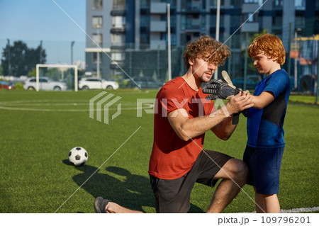 Father putting goalkeeper gloves on son hand before training football Father putting goalkeeper gloves on son hand before training football 109796201