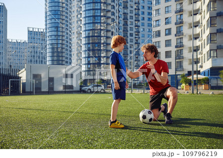 Father teaching son child to play football on city stadium Father teaching son child to play football on city stadium 109796219