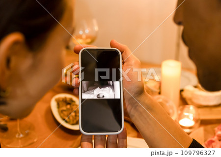 スマートフォンに映る赤ちゃんの様子を見る夫婦 109796327