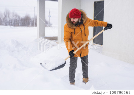 Young man clearing snow in his backyard village house with shovel. Remove snow from the sidewalk. Young man clearing snow in his backyard village house with shovel. Remove snow from the sidewalk. 109796565
