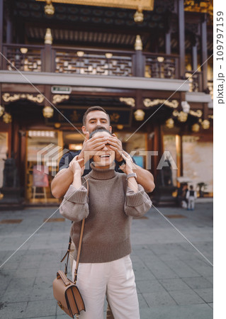 newlywed couple showing affection in Shanghai near Yuyuan. Couple take a break for some hugs while visiting China. husband and wife holding hands on the street by a market and pagoda 109797159