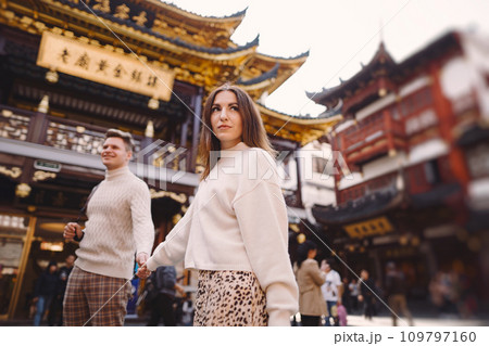 newlywed couple showing affection in Shanghai near Yuyuan. Couple take a break for some hugs while visiting China. husband and wife holding hands on the street by a market and pagoda 109797160