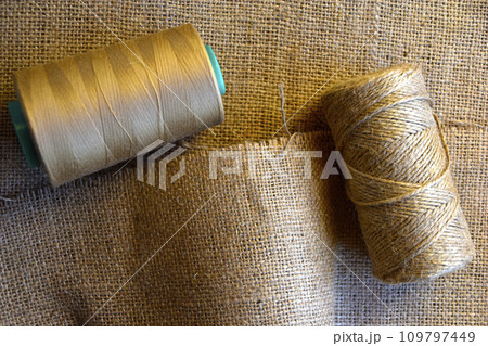 Skeins of thread on crumpled burlap. Yellow threads on coarse cloth. The material for the bags. 109797449