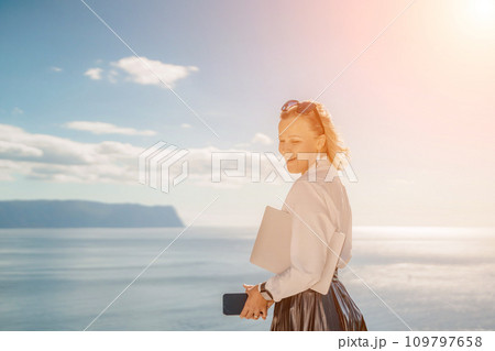 Freelance women sea working on a computer. Pretty middle aged woman with computer and phone outdoors with beautiful sea view. The concept of remote work. 109797658