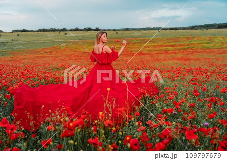 Woman poppy field red dress. Happy woman in a long red dress in a beautiful large poppy field. Blond stands with her back posing on a large field of red poppies 109797679