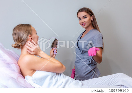 Cosmetologist advises woman. Client looks at herself in mirror. Plastic surgery and professional cosmetology. Rejuvenation procedure 109799169