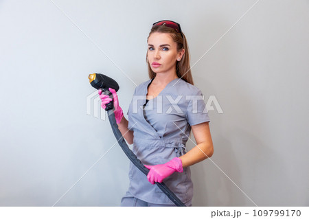 Professional cosmetologist woman holds gun from laser hair removal machine on gray background. Concept of painless hair removal 109799170