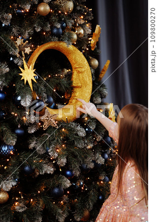Girl in a dress decorates the Christmas tree at home 109800270