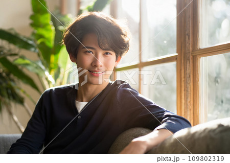 逆光の中で微笑むくせ毛の若いアジア人男性（AI生成画像） 109802319
