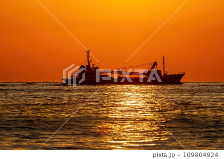 夕日を浴びながらサンロードの上を進む貨物船の情景 109804924