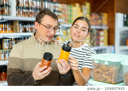 Young girl with father discussing choice of spices in supermarket Young girl with father discussing choice of spices in supermarket 109807493