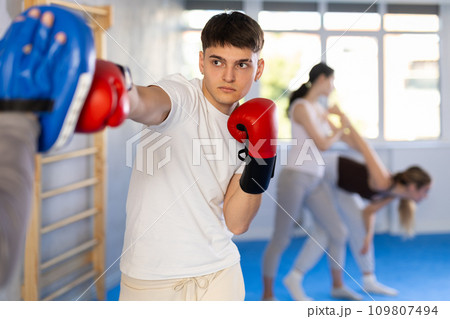 Young guy training boxing kicks on punch mitts held by instructor Young guy training boxing kicks on punch mitts held by instructor 109807494