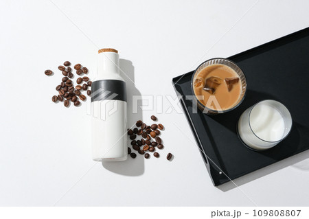 On the black tray there is a cup of milk and a cup of milk coffee, a thermos and coffee beans on a white background. Caffeine helps the body restore muscle strength and improve exercise performance. 109808807