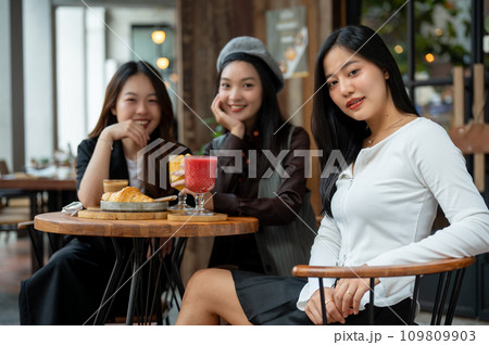 An attractive Asian woman in trendy clothes sitting at a table in a restaurant with her friends. 109809903