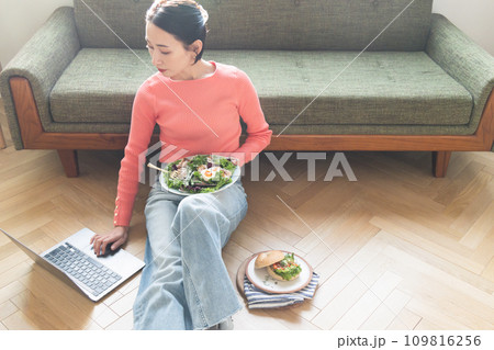 自宅で食事しながらパソコンを操作する女性 自宅で食事しながらパソコンを操作する女性 109816256