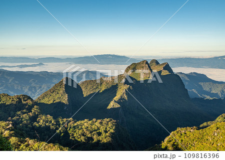 View from the top of Doi Luang Chiang Dao during a morning sunrise with trees and shrubs in the foreground and beautiful mountain ranges in background View from the top of Doi Luang Chiang Dao during a morning sunrise with trees and shrubs in the foreground and beautiful mountain ranges in background 109816396