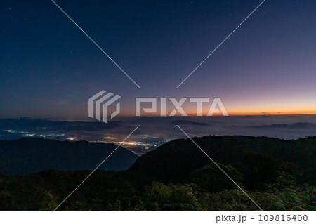 Early morning night sky from the top of Doi Luang Chiang Dao in Chiang Mai, Thailand overlooking a glowing town lights and beautiful dark blue sky with stars and glowing golden sun light at the 109816400