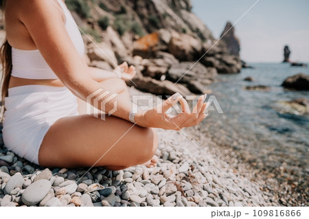 Woman sea yoga. Happy women meditating in yoga pose on the beach, ocean and rock mountains. Motivation and inspirational fit and exercising. Healthy lifestyle outdoors in nature, fitness concept. Woman sea yoga. Happy women meditating in yoga pose on the beach, ocean and rock mountains. Motivation and inspirational fit and exercising. Healthy lifestyle outdoors in nature, fitness concept. 109816866