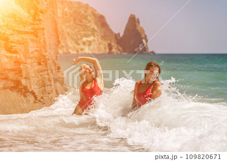 Women ocean play. Seaside, beach daytime, enjoying beach fun. Two women in red swimsuits enjoying themselves in the ocean waves. Women ocean play. Seaside, beach daytime, enjoying beach fun. Two women in red swimsuits enjoying themselves in the ocean waves. 109820671