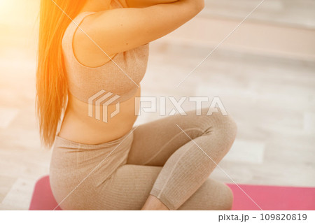 Young woman doing yoga in the gym. A girl with long hair and in a beige tracksuit stands in a cow pose on a pink carpet. A woman performs Gomukhasana. 109820819