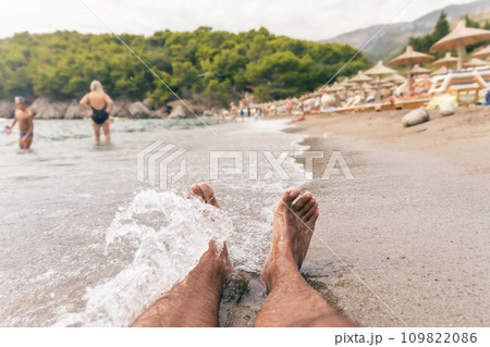 Mans feet on the beach splashed by small waves Mans feet on the beach splashed by small waves 109822086