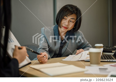 Experienced senior businesswoman discussing corporate project with colleagues at boardroom table. 109823024