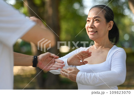 Beautiful senior woman practicing traditional Tai Chi Chuan in nature. Healthy lifestyle concept. Beautiful senior woman practicing traditional Tai Chi Chuan in nature. Healthy lifestyle concept. 109823070