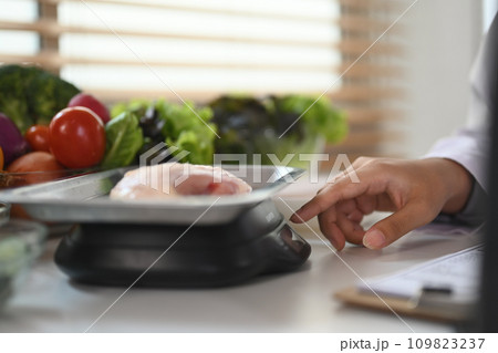Nutritionist weighing raw chicken breast on a scale during consultation in hospital. Nutritionist weighing raw chicken breast on a scale during consultation in hospital. 109823237