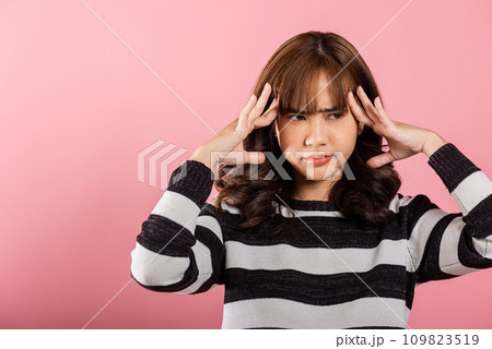 Portrait of beautiful Asian young woman sad tired strain face holding hold head by hands, stress female person unhappy closed eyes problem she headache, studio shot isolated on pink background 109823519
