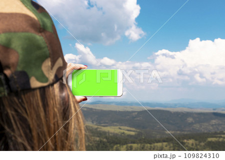 Woman photographing mountain landscape with smartphone. Empty display for copy space 109824310