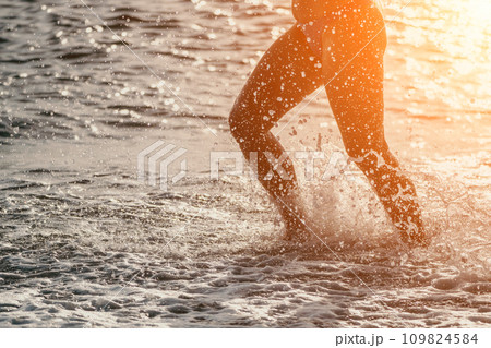 Running woman on a summer beach. A woman jogging on the beach at sunrise, with the soft light of the morning sun illuminating the sand and sea, evoking a sense of renewal, energy and health. 109824584