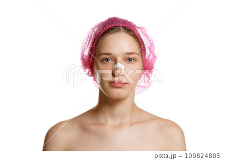 Portrait of attractive woman in pink cap with plasters on nose after rhinoplasty against white studio background. Portrait of attractive woman in pink cap with plasters on nose after rhinoplasty against white studio background. 109824805
