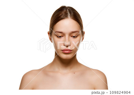 Portrait of beautiful young girl with bare shoulders, well-kept spotless skin looking down isolated white studio background 109824904