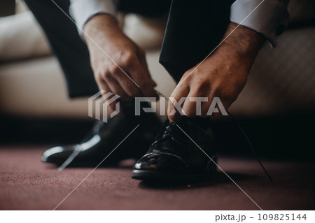 Close up of groom putting on a shoes, in the morning before wedding, tying shoelaces. Businessman getting ready for work, business meeting. Close up of groom putting on a shoes, in the morning before wedding, tying shoelaces. Businessman getting ready for work, business meeting. 109825144
