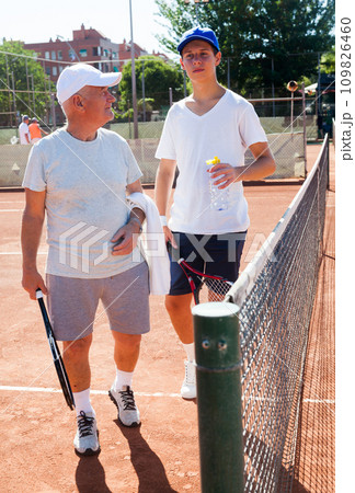 Grandfather and grandson talking on court playing tennis 109826460