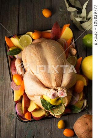 A large chicken stuffed with an apple with vegetables and citrus fruits, top view A large chicken stuffed with an apple with vegetables and citrus fruits, top view 109829777