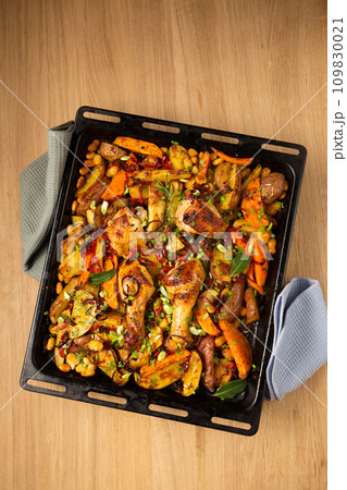 Baked vegetables with ruddy baked chicken on a large metal griddle, copy space 109830021