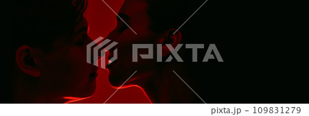 Young man and woman, couple standing closely to each other, almost kissing against red background in neon light. Monochrome Young man and woman, couple standing closely to each other, almost kissing against red background in neon light. Monochrome 109831279