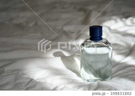 Male blue perfume bottle on the white bed with shadows Male blue perfume bottle on the white bed with shadows 109831802
